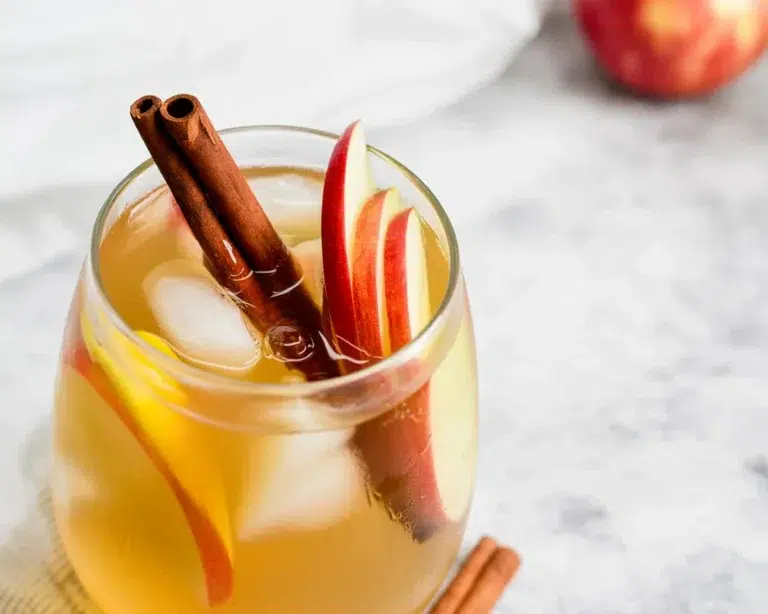 Bourbon Apple Cider Sangria in a glass with apples, cinnamon sticks, and red wine.