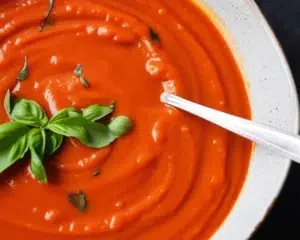 Bowl of homemade roasted tomato basil soup garnished with fresh basil leaves.