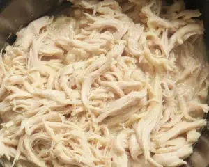 Crockpot Shredded Chicken cooking in a slow cooker with seasonings and broth.