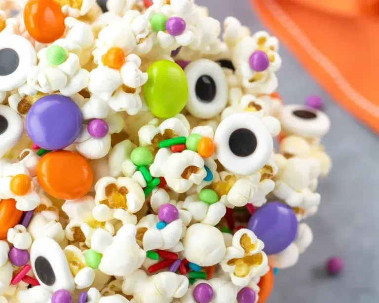 Colorful Halloween popcorn trail mix with pretzels, candy corn, and sprinkles in a bowl.