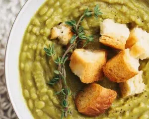 Bowl of hearty split pea soup with ham, carrots, and celery, perfect for winter meals.