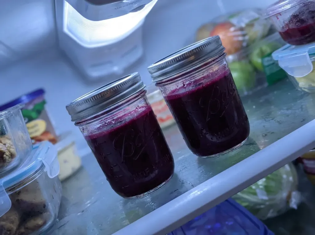 two small glass mason jars of deep purple beet celery juice stored in refrigerator for two day batch prep