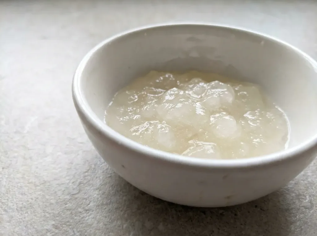 Unflavored gelatin powder blooming in cold water in a small white bowl on kitchen counter