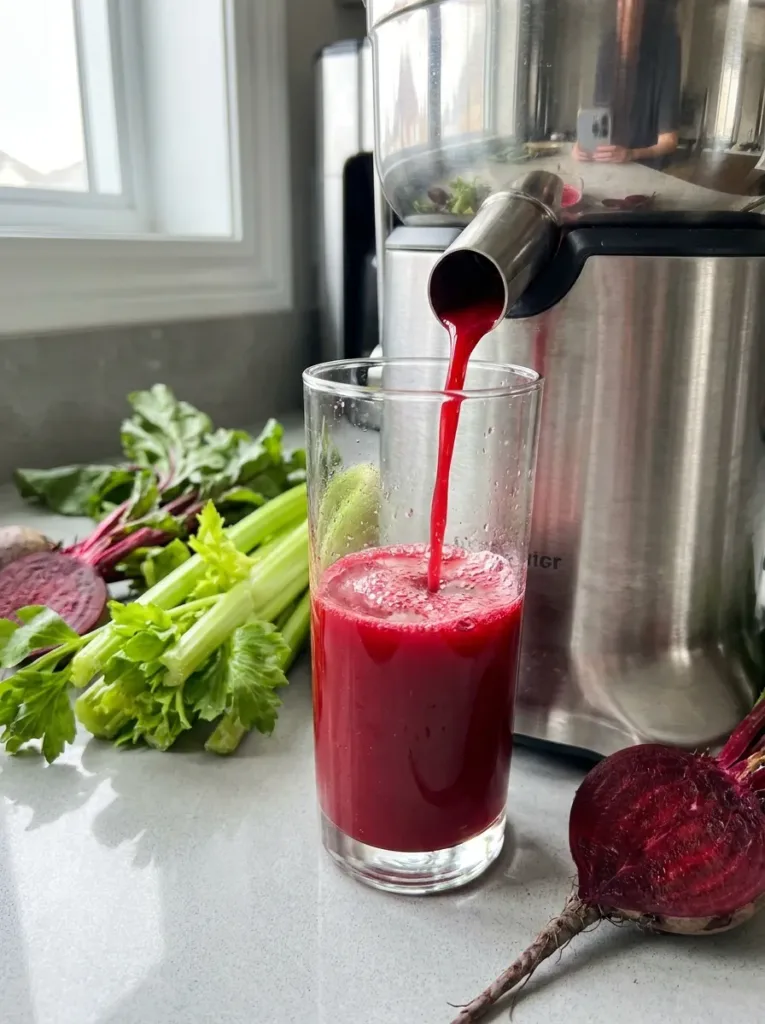 Bright red juice pouring from juicer into glass with celery beside it